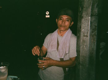 Portrait of mid adult man with drink standing by pole at night