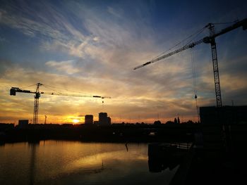 Silhouette cranes at construction site against sky during sunset