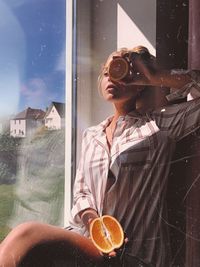 Young woman with halved citrus fruit sitting by window at home