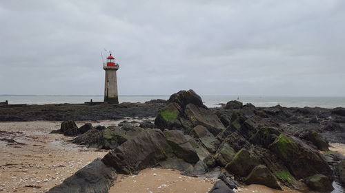 Lighthouse on beach by sea against sky