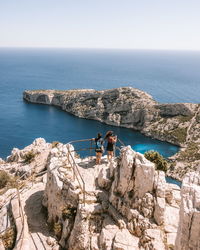 People on rock by sea against sky