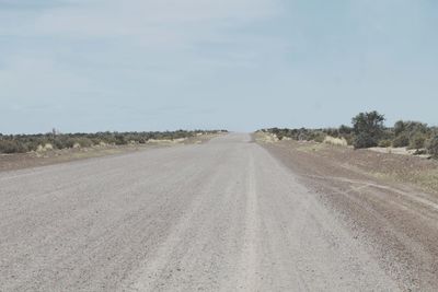 Dirt road amidst field against sky