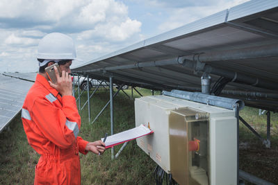 Side view of worker talking on phone while standing by solar panel