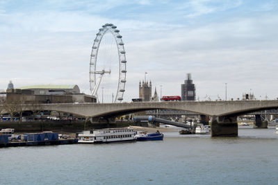 Bridge over thames river in city against cloudy sky