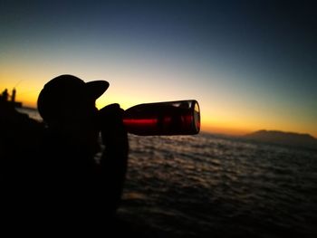 Silhouette woman photographing sea against sky during sunset