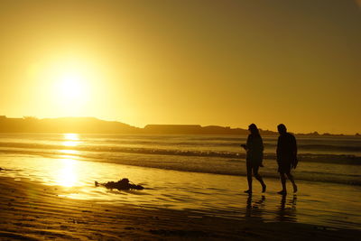 Silhouette couple on beach against sky during sunset