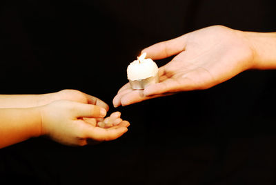 Close-up of hand holding illuminated lamp over black background