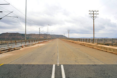 Empty road against cloudy sky on sunny day