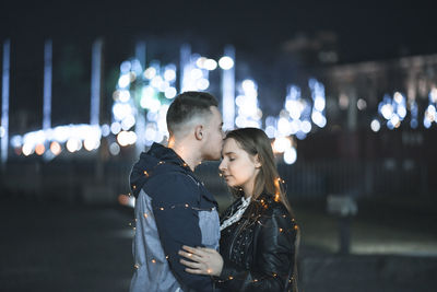 Friends standing against illuminated city at night