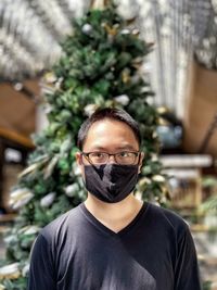 Portrait of young man in eyeglasses and face mask against christmas tree and skylight.