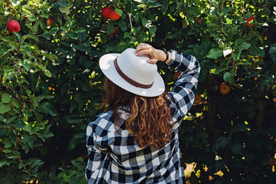 Rear view of woman wearing hat standing against plants