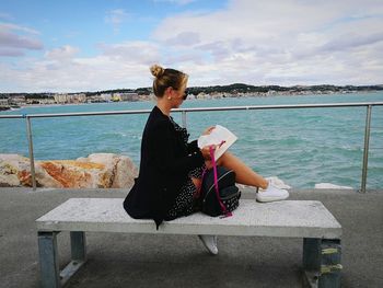 Woman sitting on seat at promenade against sky