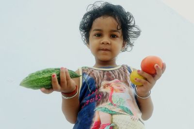 Portrait of cute girl holding fruit against white background