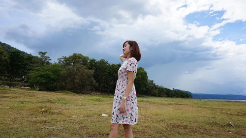 Side view of young woman standing on field against sky