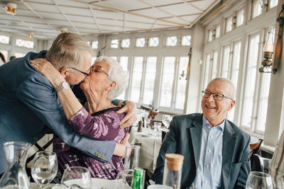 Senior couple kissing while male friend smiling in restaurant