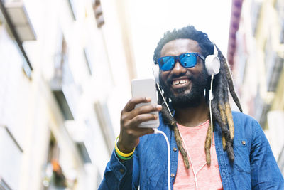 Smiling young man wearing sunglasses listening music on headphones in city