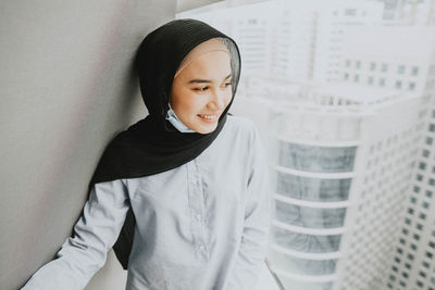 Portrait of smiling young woman standing against wall