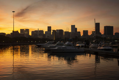 Boats in river by buildings against sky during sunset