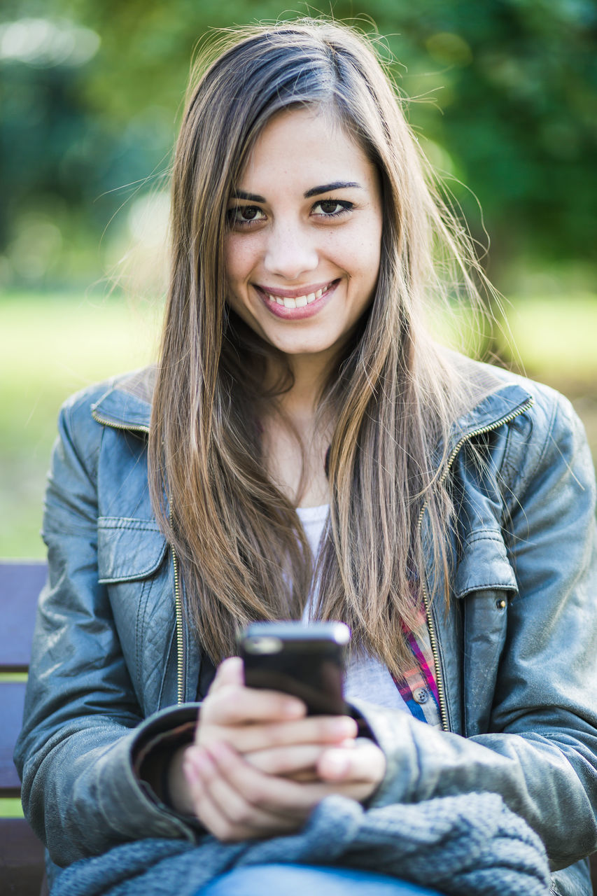 Portrait of smiling young woman using mobile phone in park