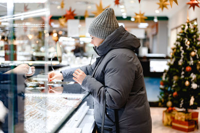 A young woman in a gray jacket and hat chooses a ring for herself in a jewelry store. christmas sale 