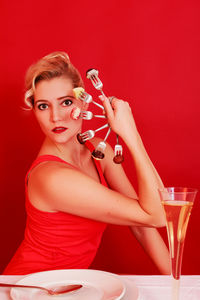 Portrait of woman holding forks with chocolates at table against red background
