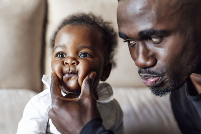 Playful father squeezing baby girl's cheeks at home