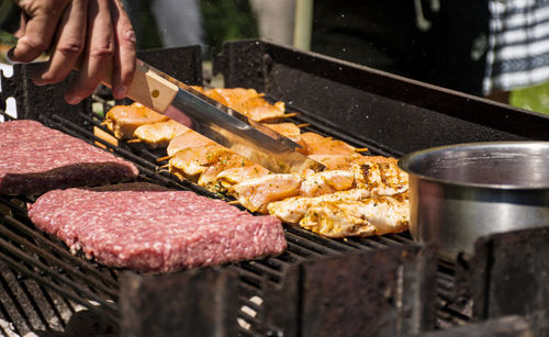 Close-up of man holding utensil and grilling meat in back yard.