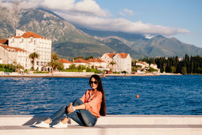 Portrait of smiling woman sitting on retaining wall against lake