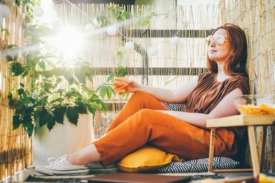 Young stylish woman sitting and holding cocktail on modern terrace.