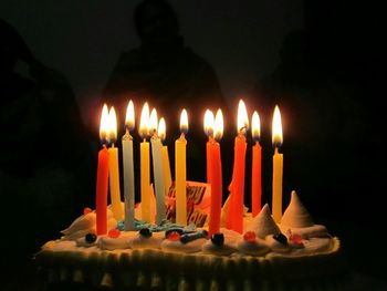 Close-up of lit candles on birthday cake in darkroom
