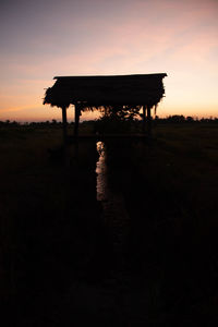 Silhouette built structure on field against sky during sunset