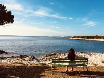 Rear view of woman sitting on bench against sea