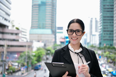 Portrait of smiling businesswoman holding file with buildings in background