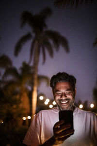 Low angle view of happy man using phone against clear sky during sunset