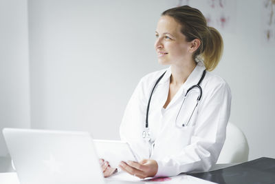 Smiling doctor looking away while holding digital tablet at clinic