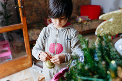 Child in overall decorating the christmas tree with golden bell