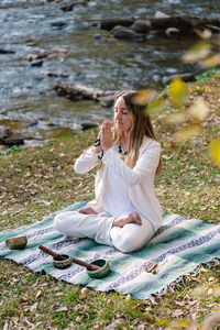 Young woman drinking water while sitting on rock