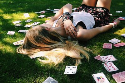 Woman lying on grass surrounded with cards