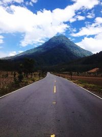 Empty road by mountains against cloudy sky