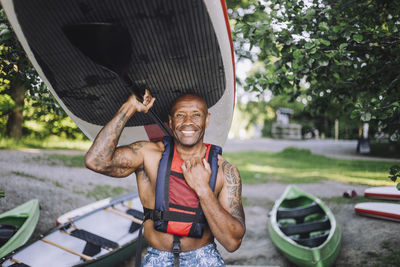 Portrait of smiling man carrying paddleboard and oar