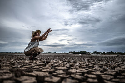 Woman crouching on arid land against sky during sunset