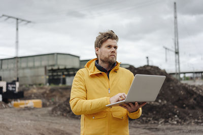 Man holding laptop, construction site in the background