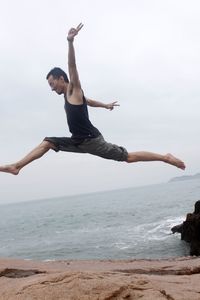 Low angle view of man jumping at beach against sky