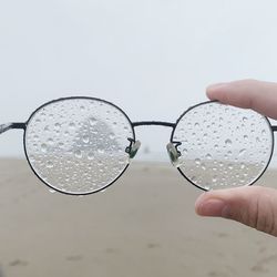 Cropped hand holding wet eyeglasses at beach