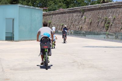 Rear view of people riding bicycle on street during sunny day