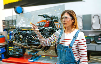 Female mechanic using hud panel screen with augmented reality hologram to review motorcycle