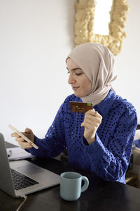 Woman in headscarf paying bills online at home