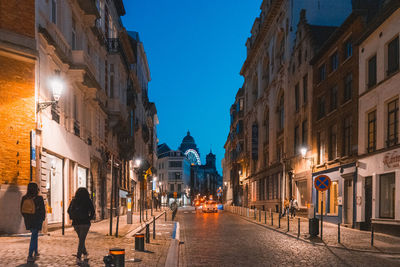 People walking on street amidst buildings in city. night in brussels, belgium 