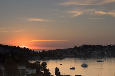 Silhouette cityscape by sea against sky during sunset