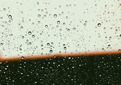 Close-up of raindrops on windshield against sky during sunset